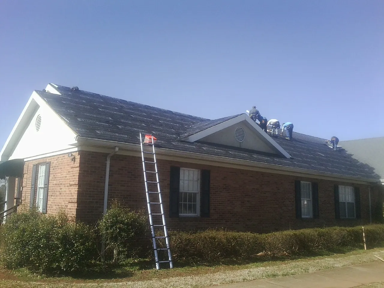 Crew tearing shingles off a brick ranch roof with a ladder set — Emergency Roof Repair work by our crew in Beulah